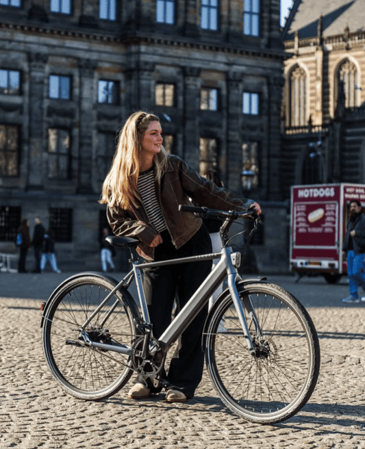 Vrouw met een elektrische fiets op een plein, ideaal voor gratis proefrit elektrische fiets.